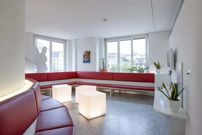 A bright, welcoming dental clinic waiting room with red leather seating and glowing cube tables.