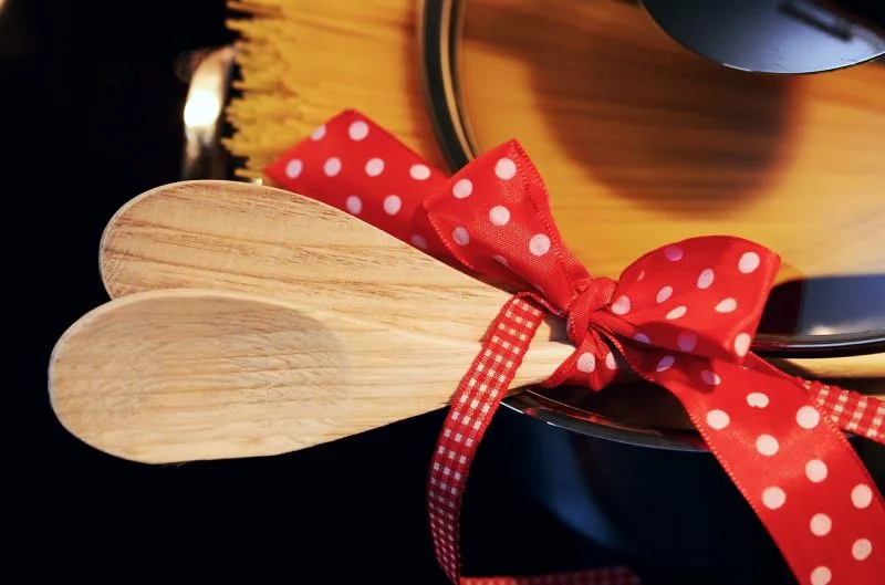 Wooden spoons bound by a cheerful red polka-dot bow beside a cooking pot.