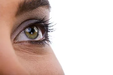 Close-up of a woman's green eye with natural lashes against a white background.