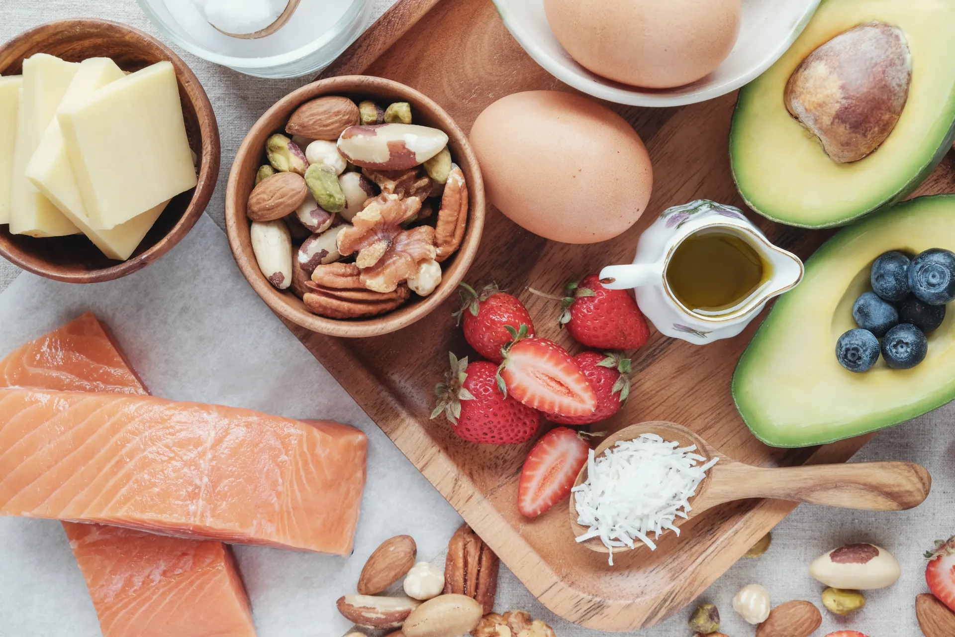 A colorful spread of healthy whole foods including salmon, avocado, nuts, eggs, and berries.