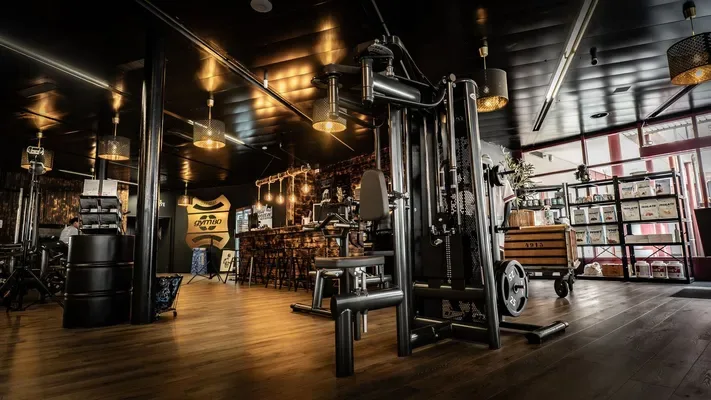 Cable machine station with rustic bar area in background, capturing the unique blend of training space and community gathering central to the studio's identity.
