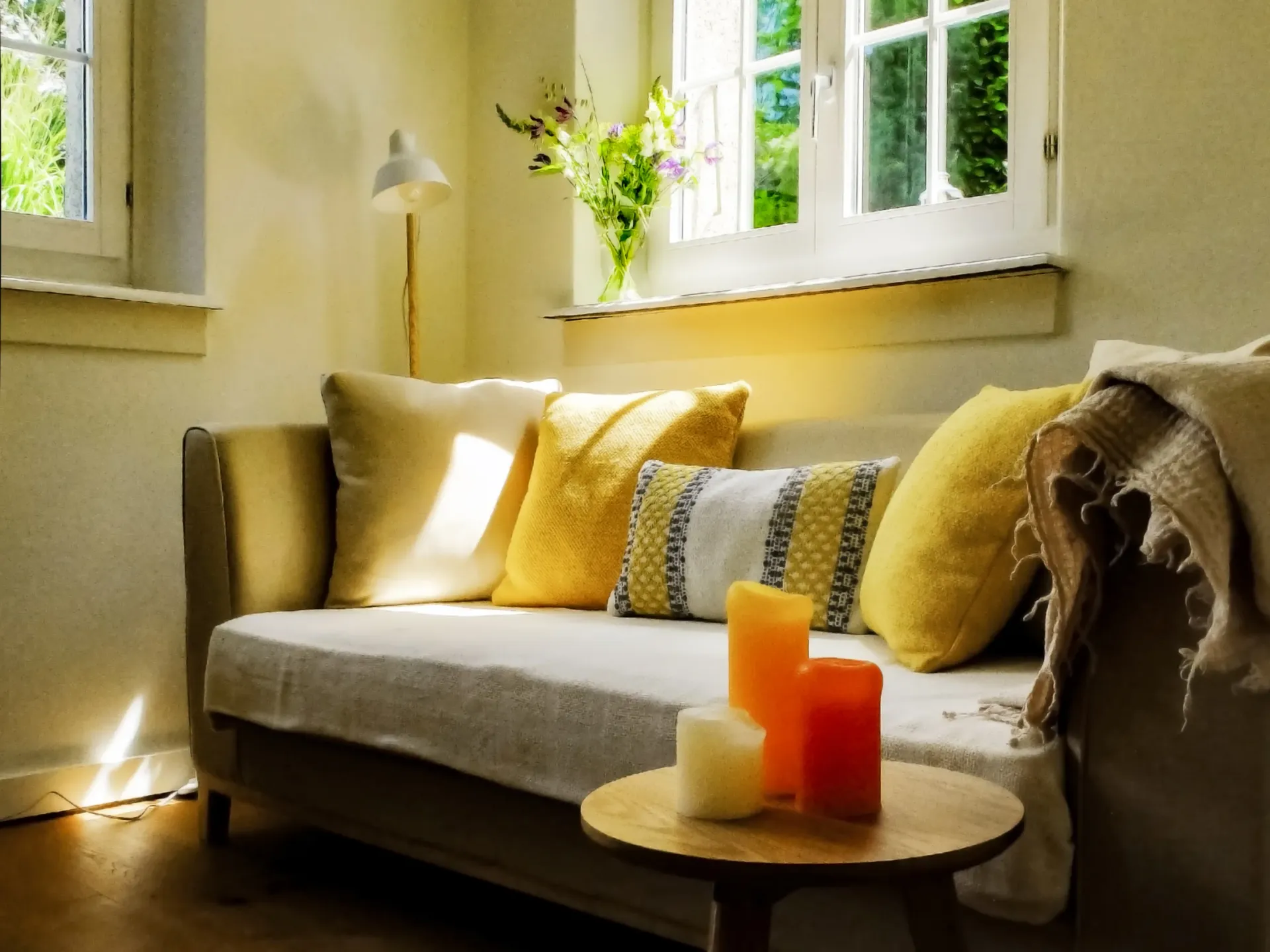 Warm, sunlit therapy room with couch, candles, and fresh flowers — conveys the safe, welcoming space where clients can let go and arrive.