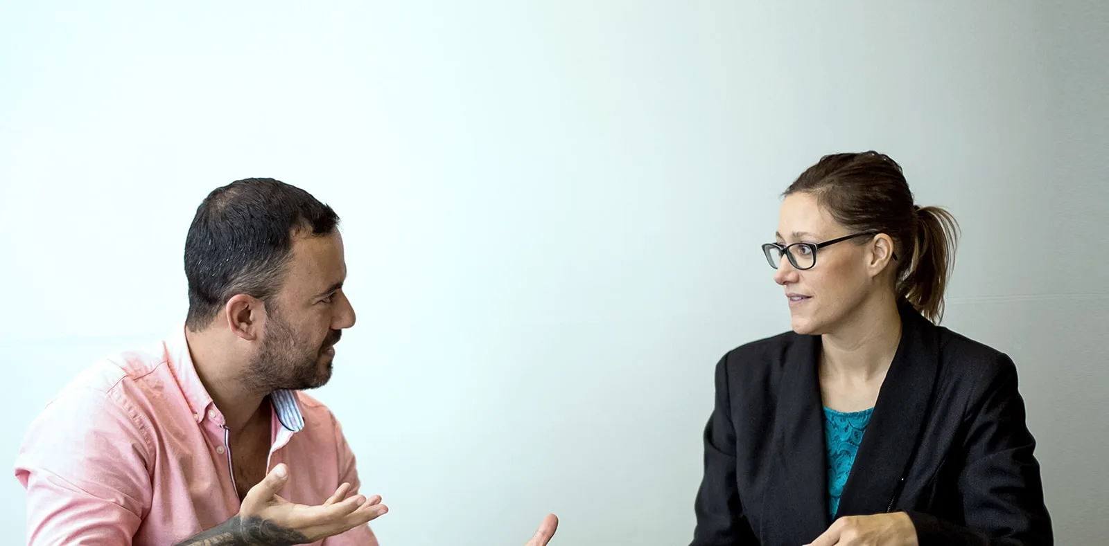 Woman with ponytail and glasses speaks one-on-one with a man in a professional coaching conversation.