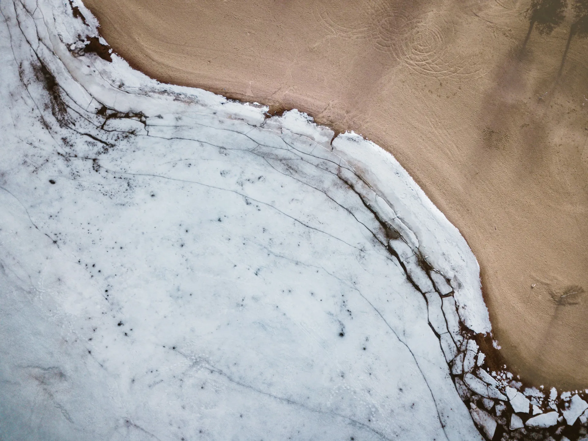 Aerial view of melting ice meeting sandy ground, evoking seasonal transition and natural harmony.