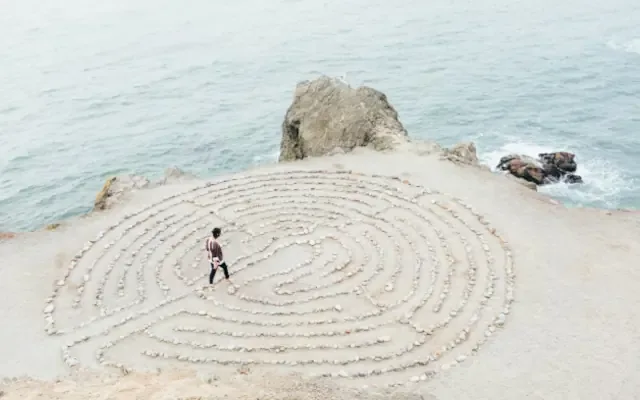 A person walks meditatively through a stone labyrinth on a coastal clifftop above the sea.
