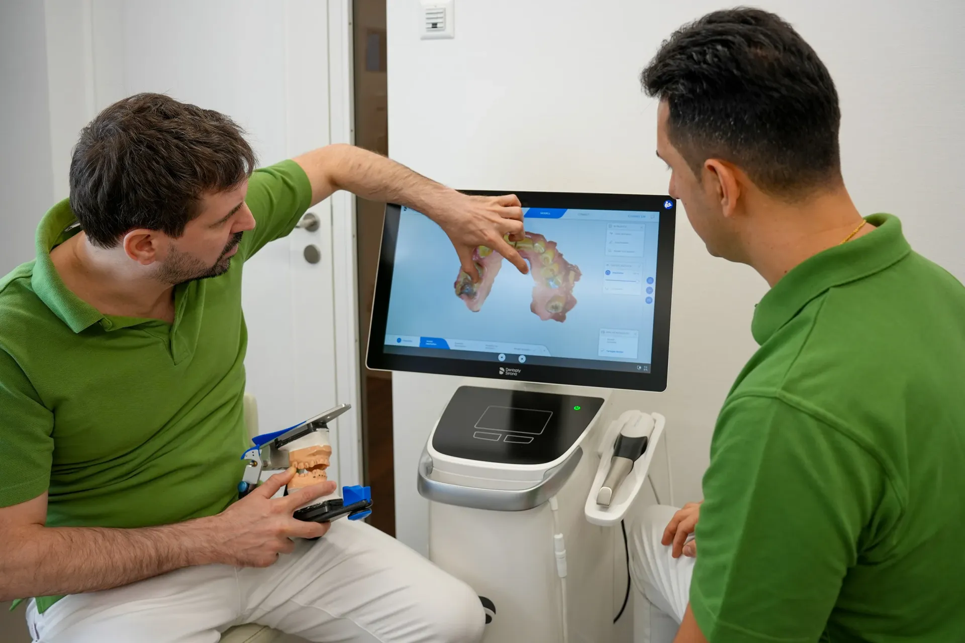 Two dental professionals in green uniforms smile warmly while reviewing a dental model together in a modern clinic.