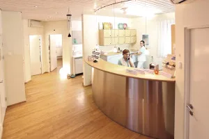 Staff members interact at a curved modern reception desk in a bright, open dental practice.