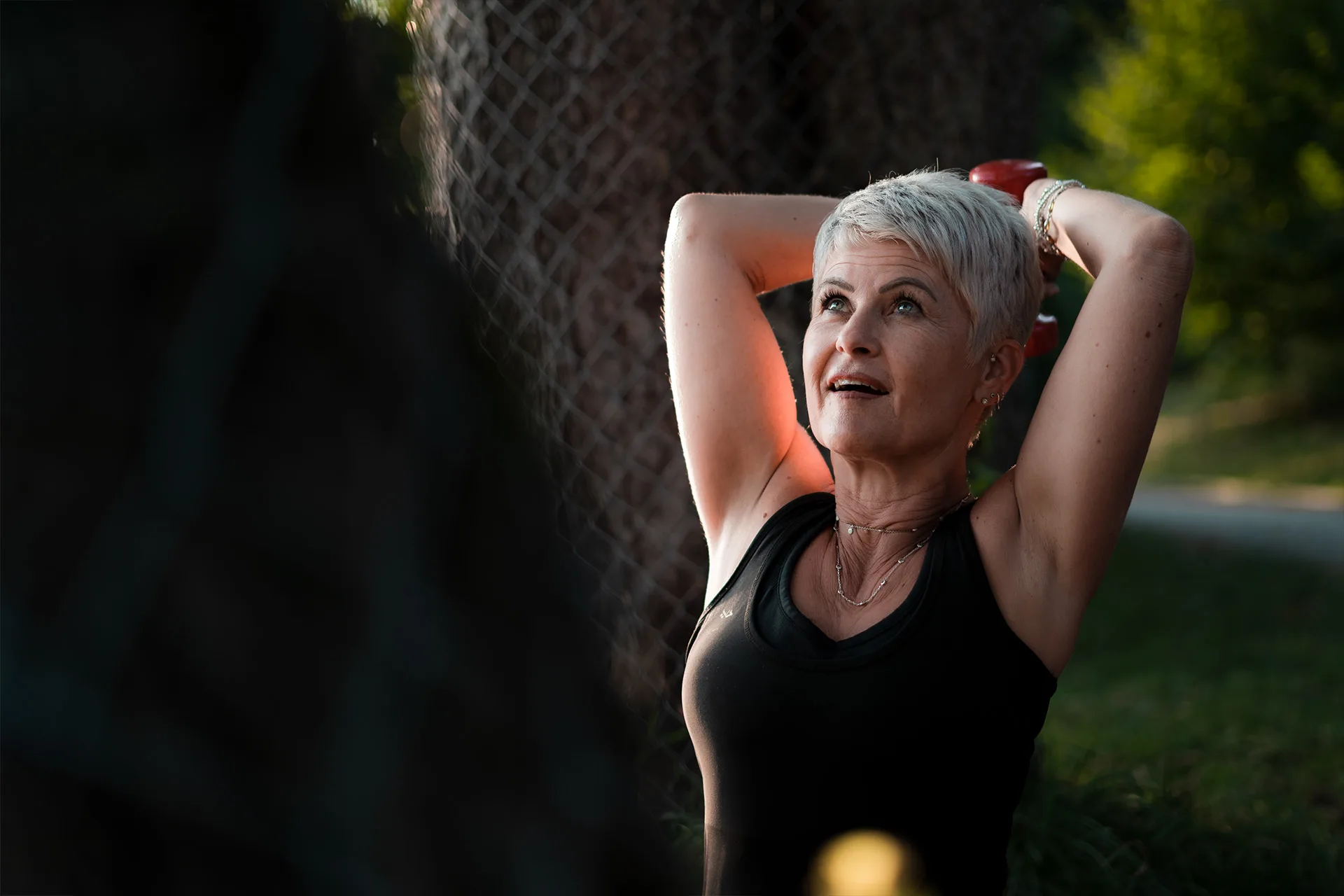 The silver-haired trainer works out outdoors with a dumbbell at golden hour, embodying the passionate, energetic spirit of FIT-N-FUN.