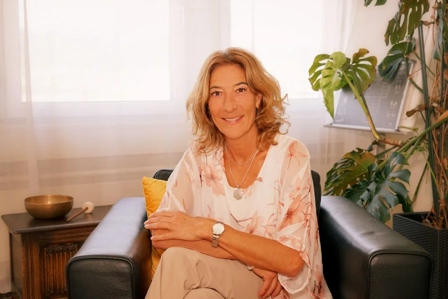 Gerda Vontobel sits relaxed and smiling in her bright coaching office surrounded by plants.
