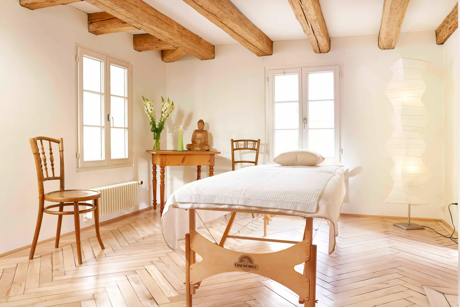 Serene treatment room with exposed beams, massage table, Buddha statue, and natural light.