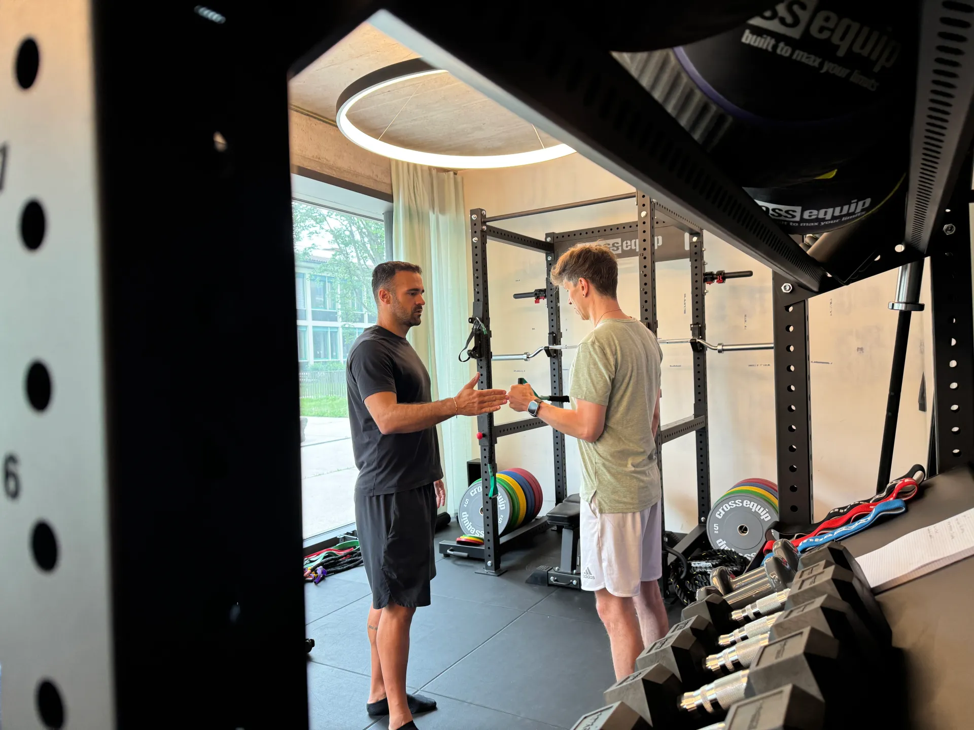 Two trainers consulting with client in bright, minimalist gym space showcasing personalized coaching approach.