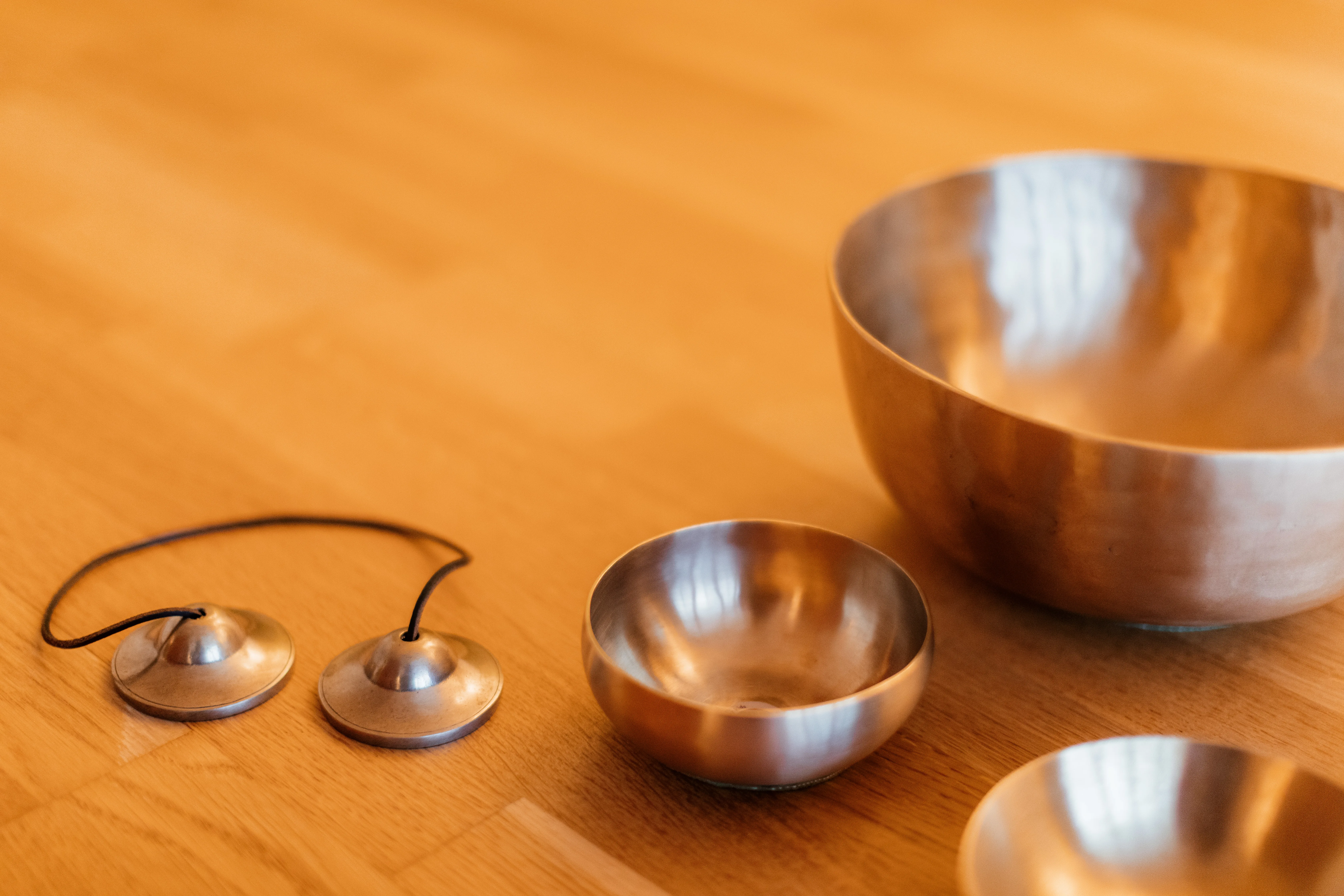 Close-up of Tibetan singing bowls and tingsha cymbals resting on a wooden floor.