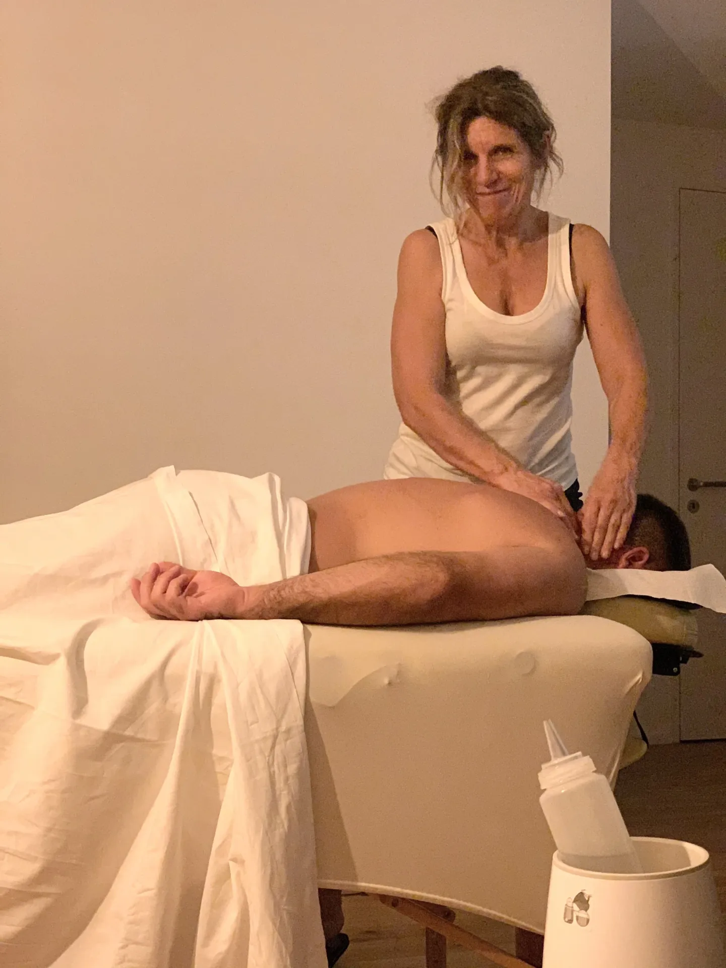Beatrice performs a back massage on a client lying on a treatment table in a cozy room.
