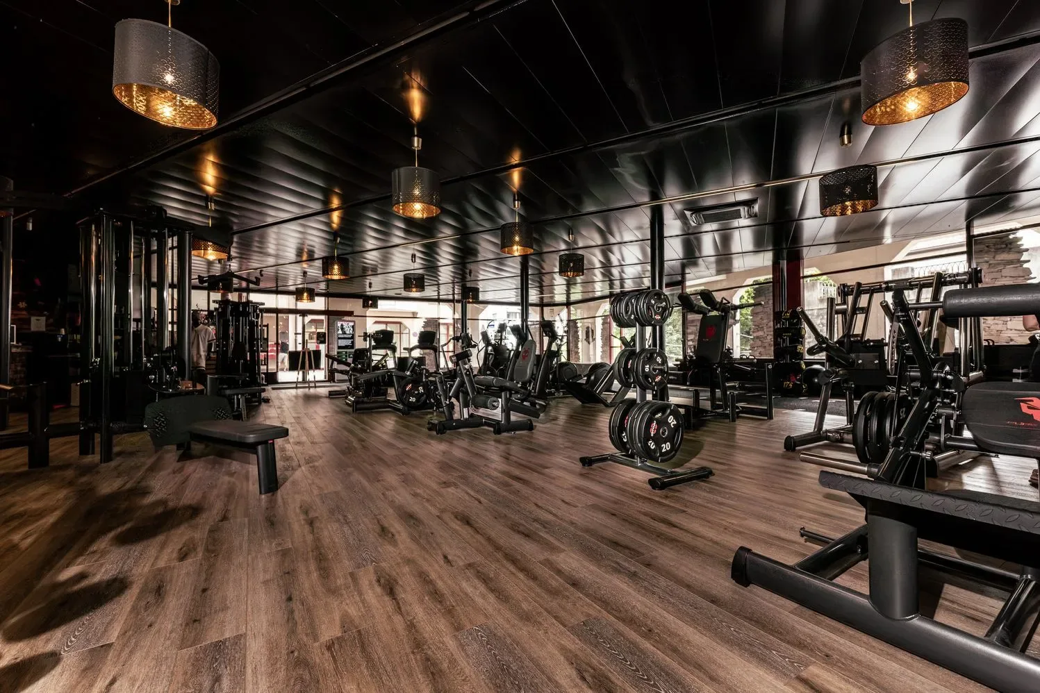 Spacious, warmly lit training floor with premium black equipment and wood flooring, showcasing the welcoming, high-quality atmosphere of the studio.