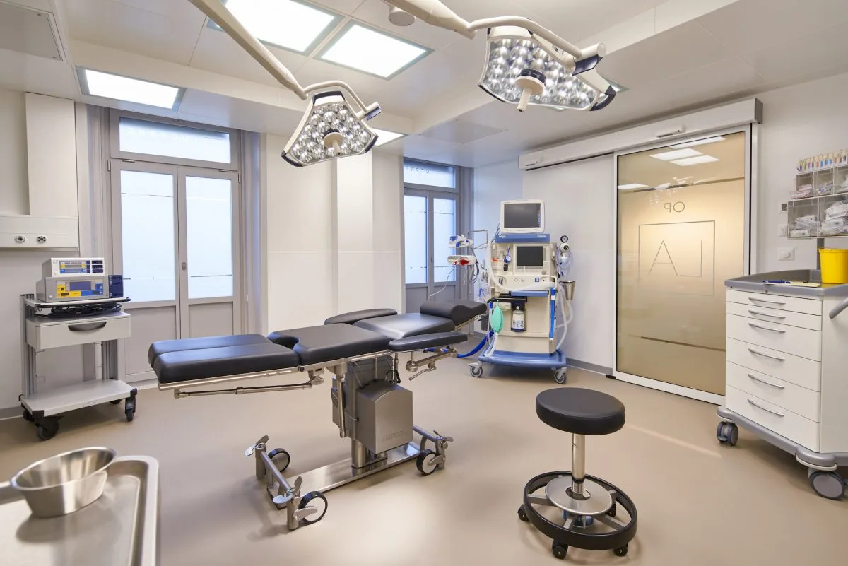 Modern clinic corridor with glass-walled treatment room and medical recliner chair visible.