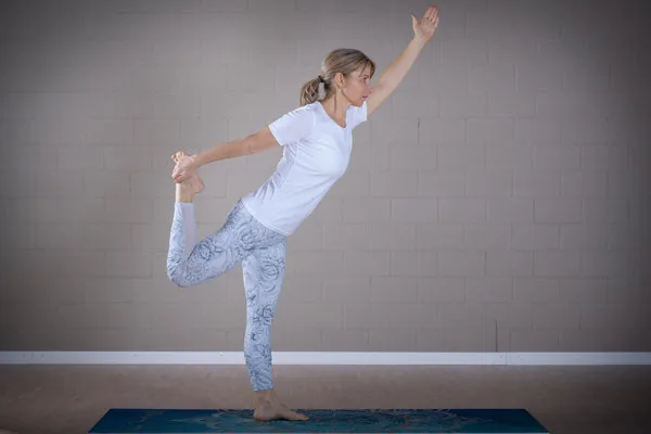 A woman performs an advanced standing balance pose, holding her foot behind her.