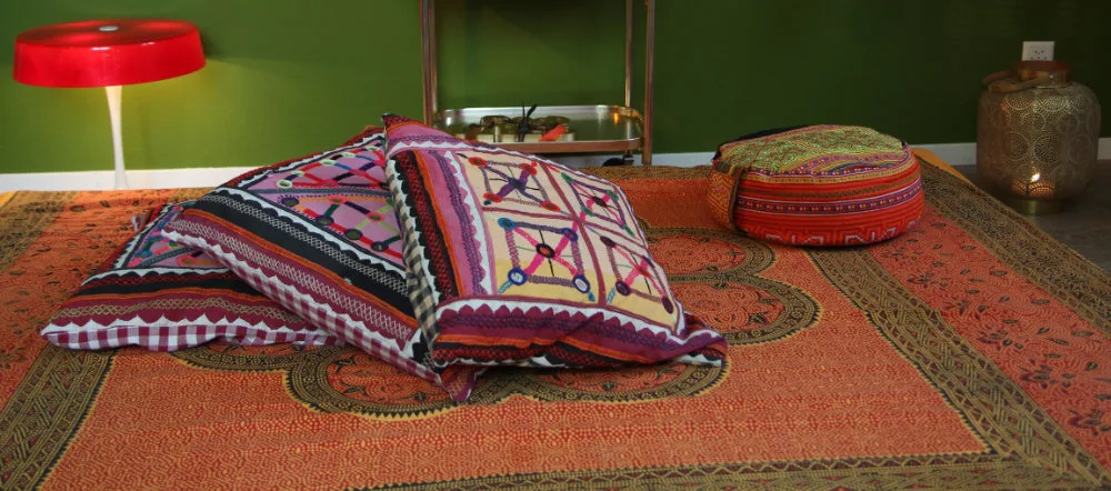 A warmly decorated meditation space with colorful ethnic cushions on an ornate orange rug.