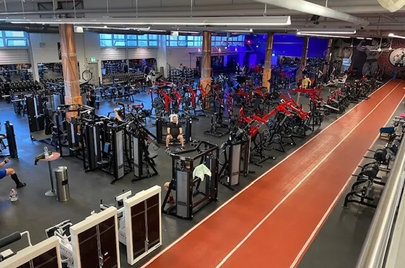 Overhead view of a large gym floor with red strength machines and an indoor running track.