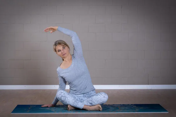 A woman balances gracefully in tree pose on a yoga mat in a studio.