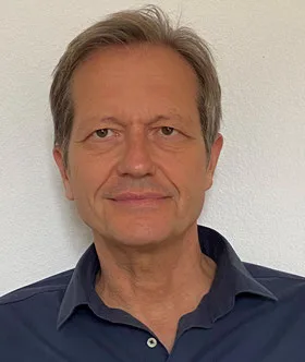 A professional portrait of Andreas Fuchs, the therapist, in a dark blue shirt against a neutral background.