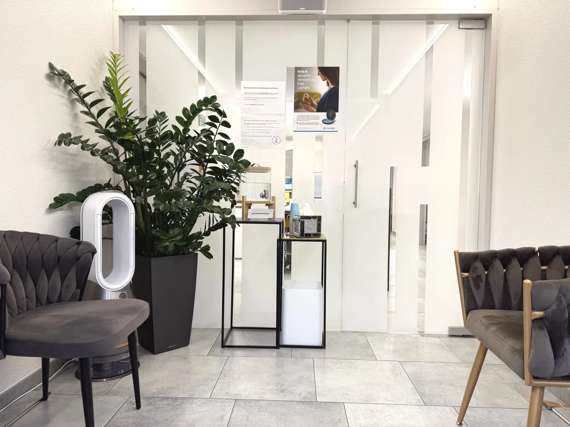 The modern practice waiting area features velvet chairs, a large plant, and glass doors.