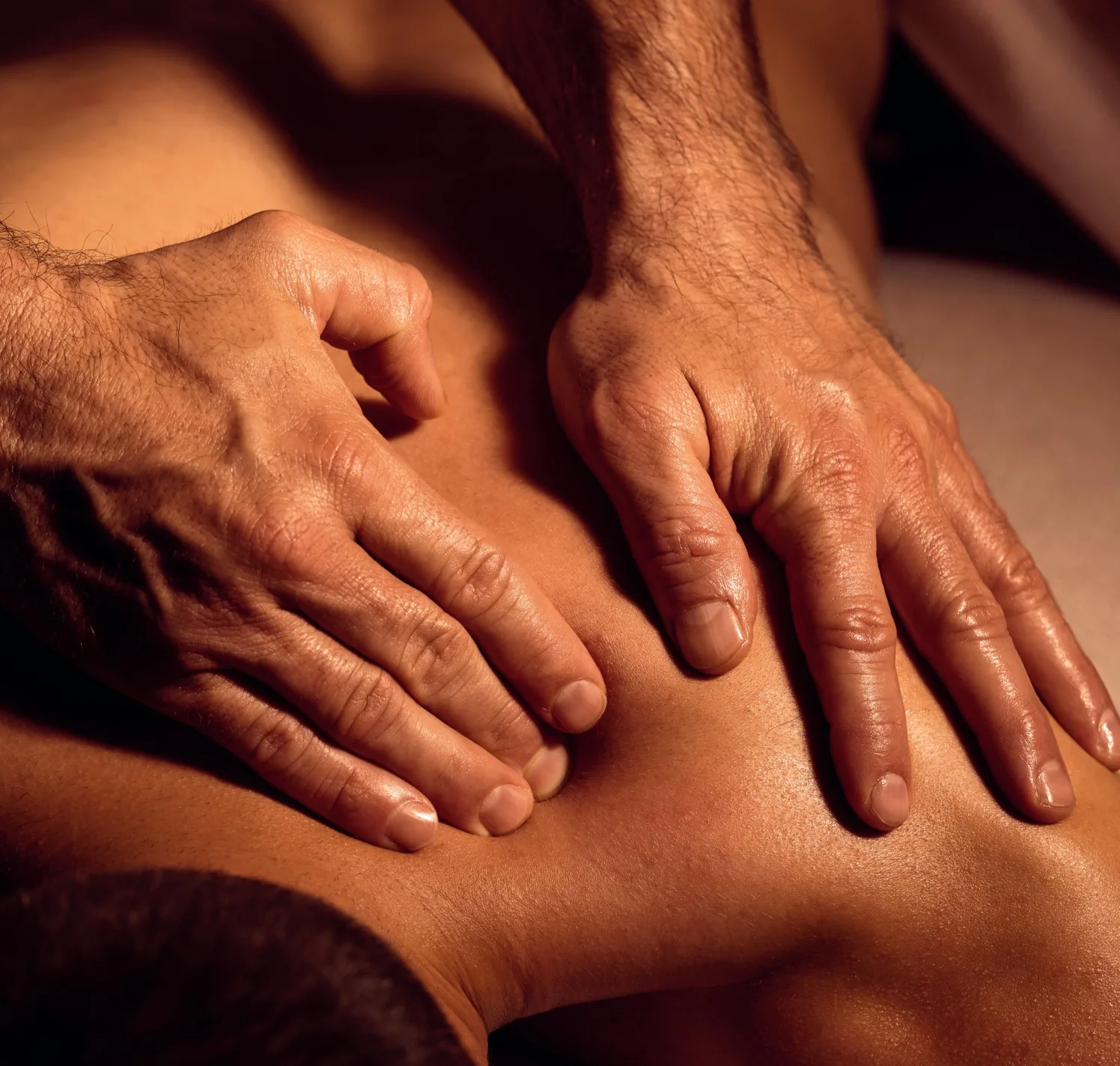 Therapist applying firm bilateral pressure across a client's oiled upper back.