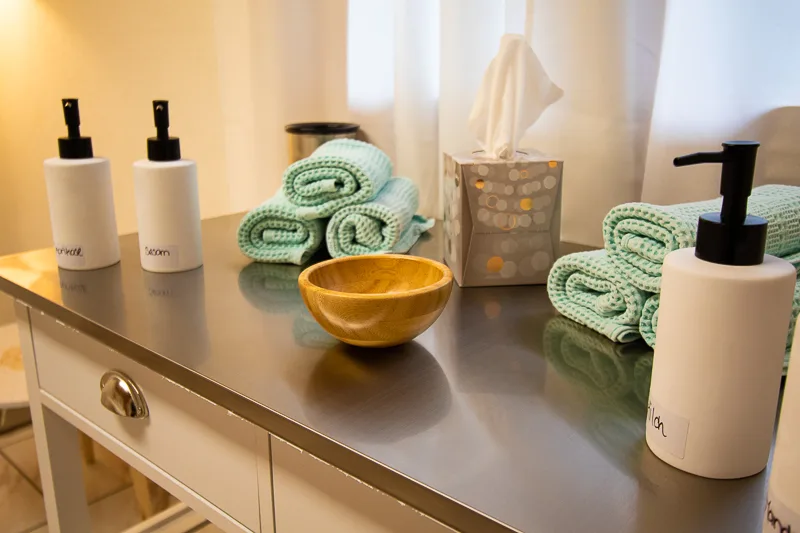 Neatly arranged spa counter with lotion bottles, rolled mint towels, a wooden bowl, and a tissue box.