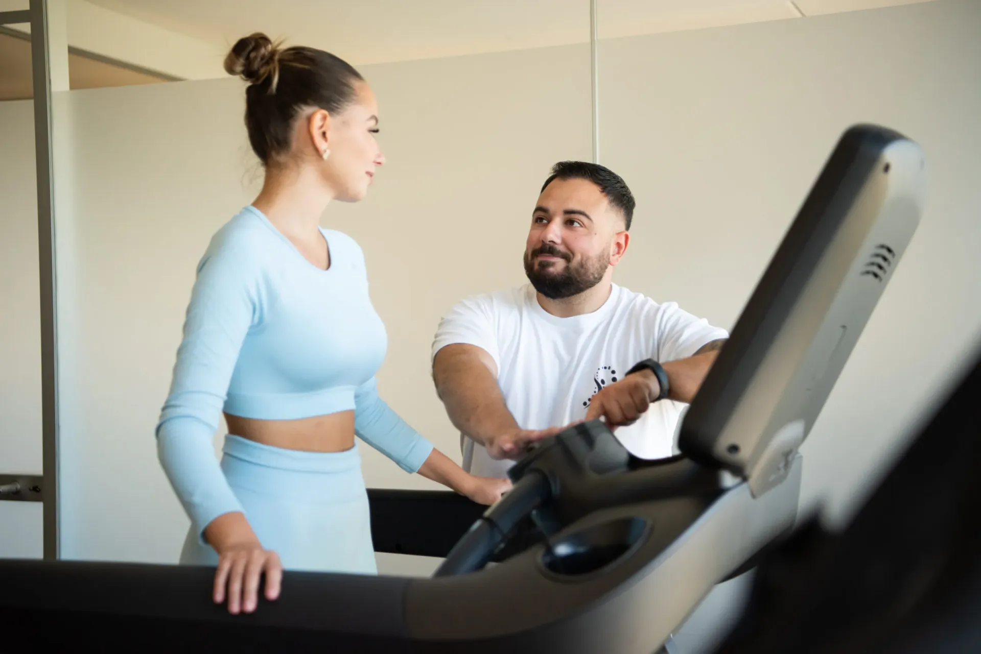 A physiotherapist in a white shirt guides a female patient walking on a treadmill.