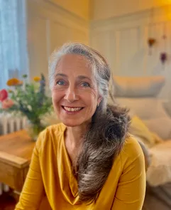 Anja Scheib smiling warmly indoors wearing a yellow top in a cozy room.