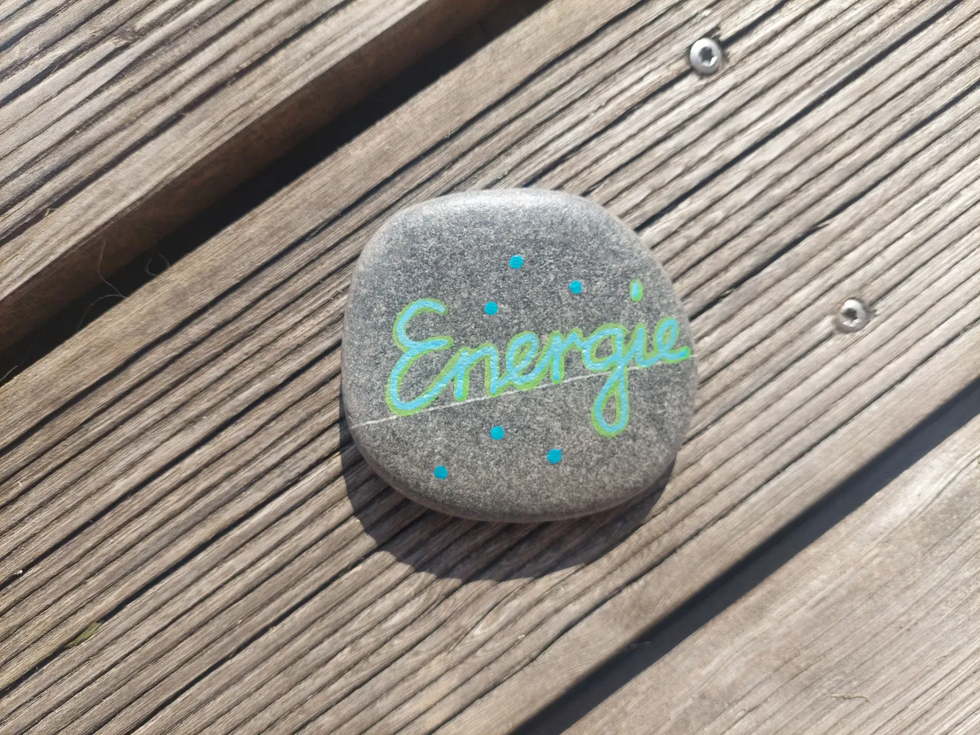 A painted stone inscribed with 'Energie' rests on wooden planks, symbolizing personal strength.
