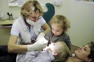 A dentist gently examines a child patient while the mother holds the child, showing warm family care.
