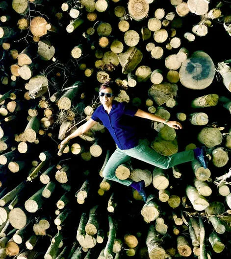 A man lying spread-eagled atop a large pile of freshly cut logs, viewed from above.