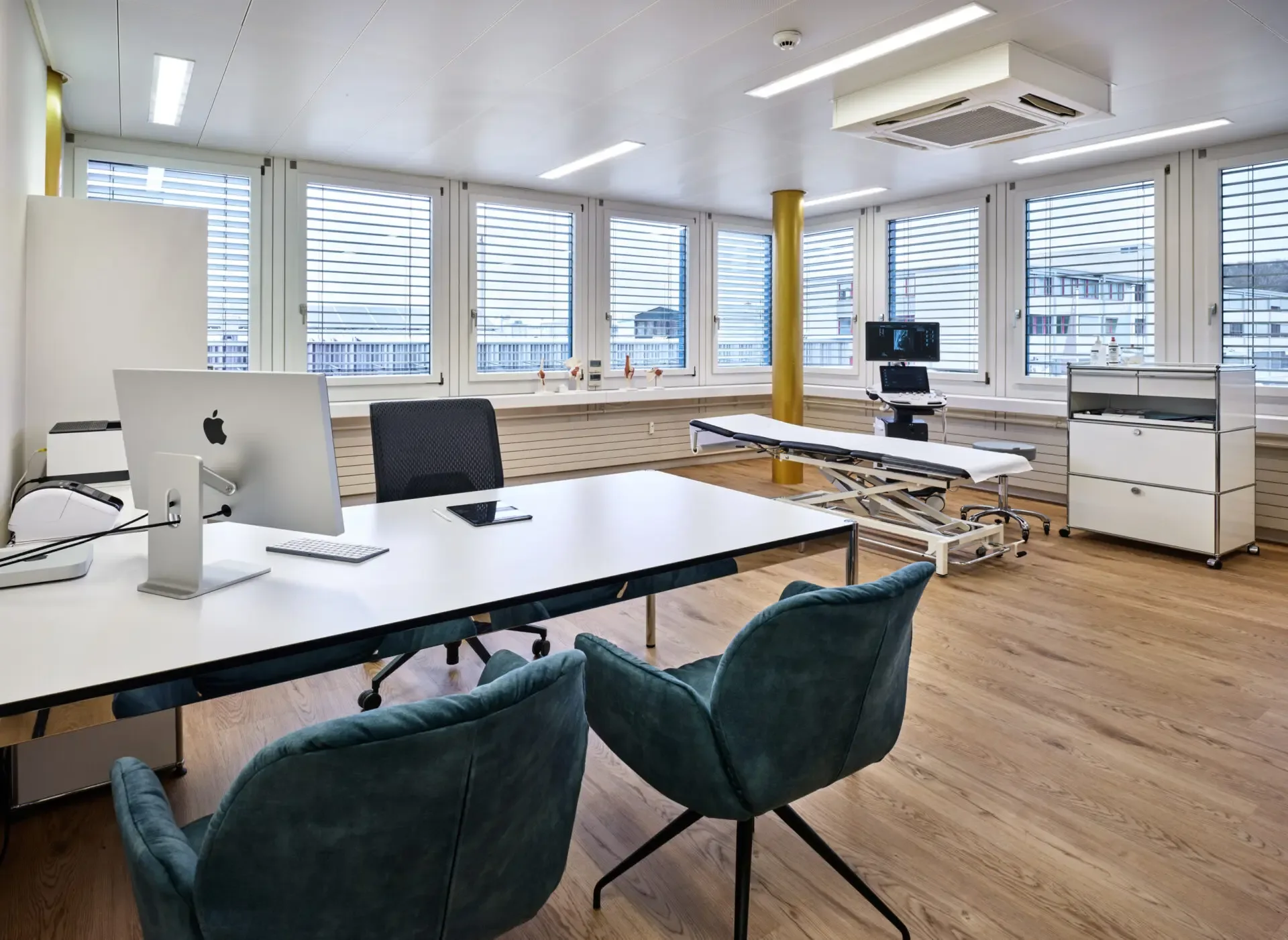 Bright, modern consultation room with Apple iMac, examination table and ultrasound equipment, showcasing the practice's state-of-the-art medical infrastructure.