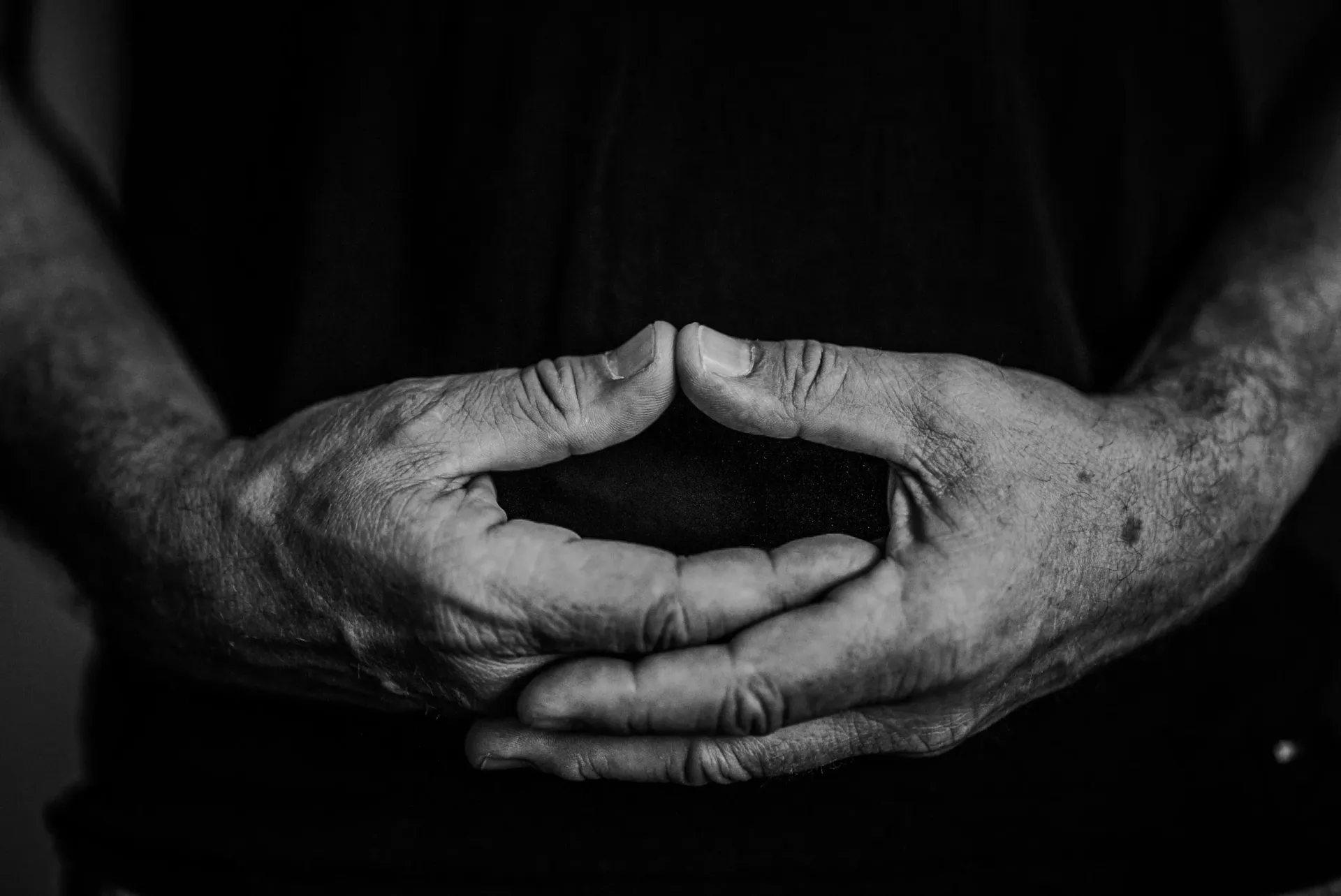 Intimate close-up of weathered, clasped hands in black and white, symbolizing decades of practice, experience, and the meditative stillness central to the studio's philosophy.