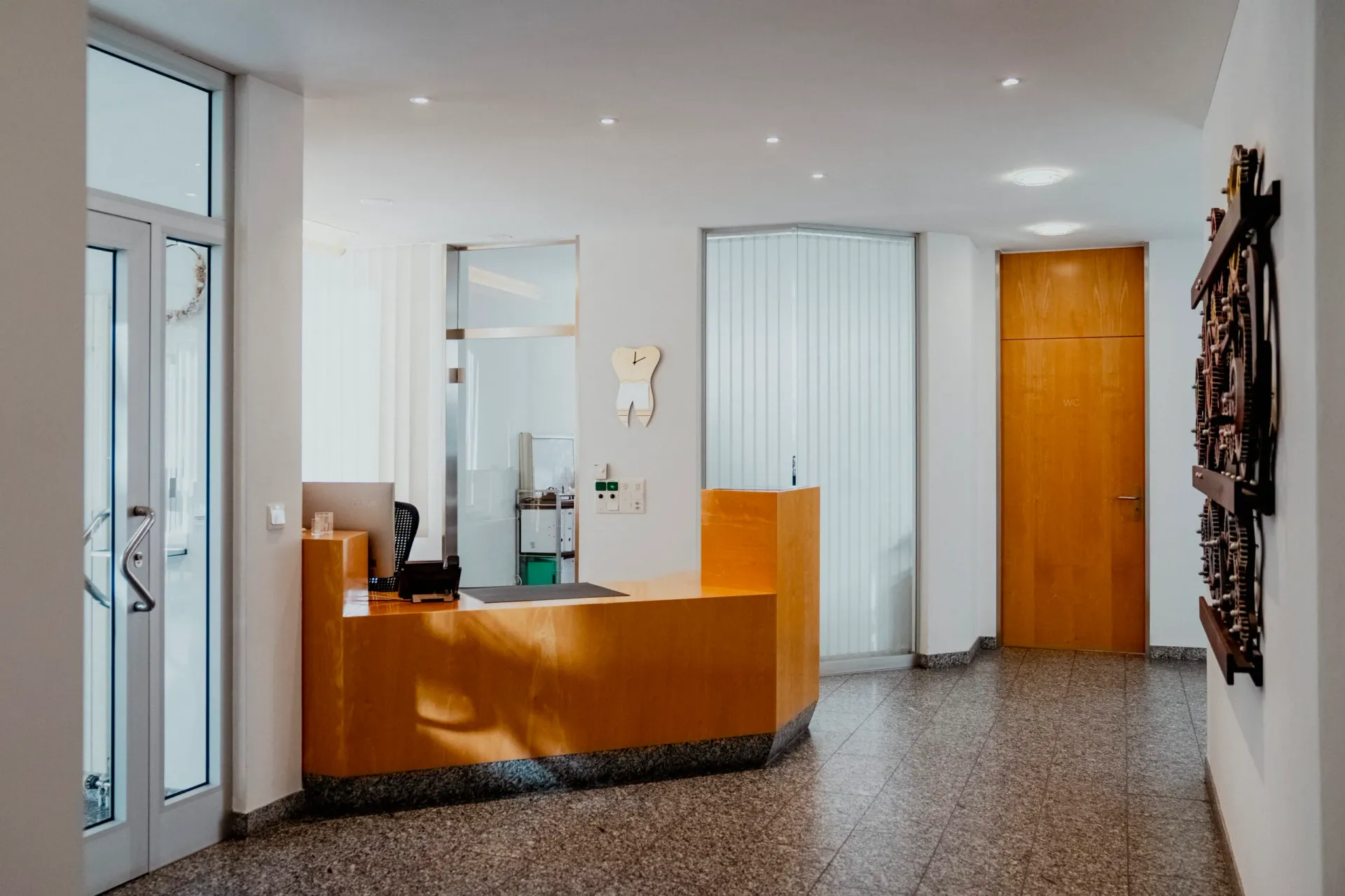 Modern glass-and-steel entrance of the Zahnarztpraxis Per Nielsen building, surrounded by Alpine landscape, conveying a welcoming, professional first impression.