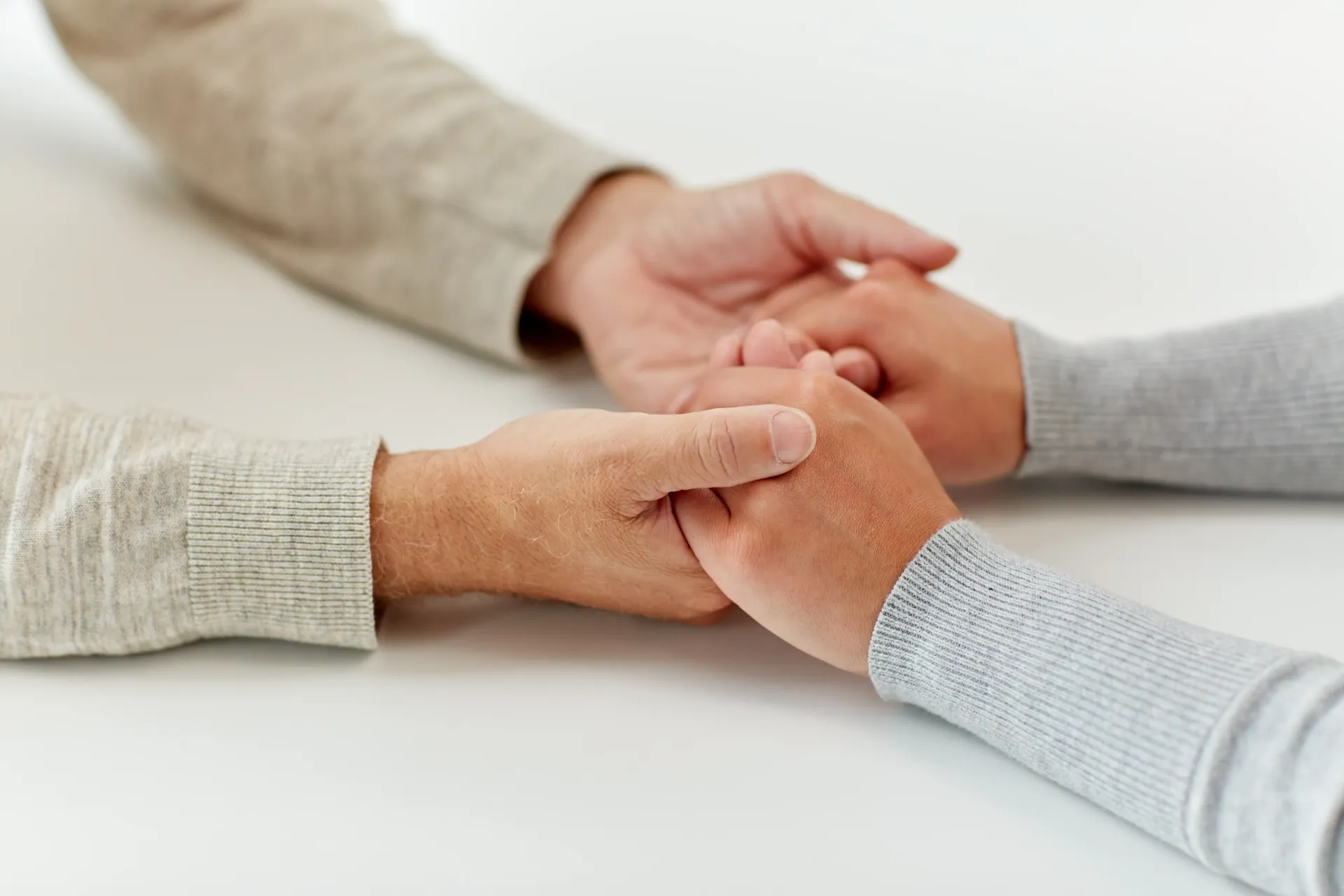 Two people gently holding hands across a table, visually representing the empathetic patient-doctor relationship at the heart of this article.