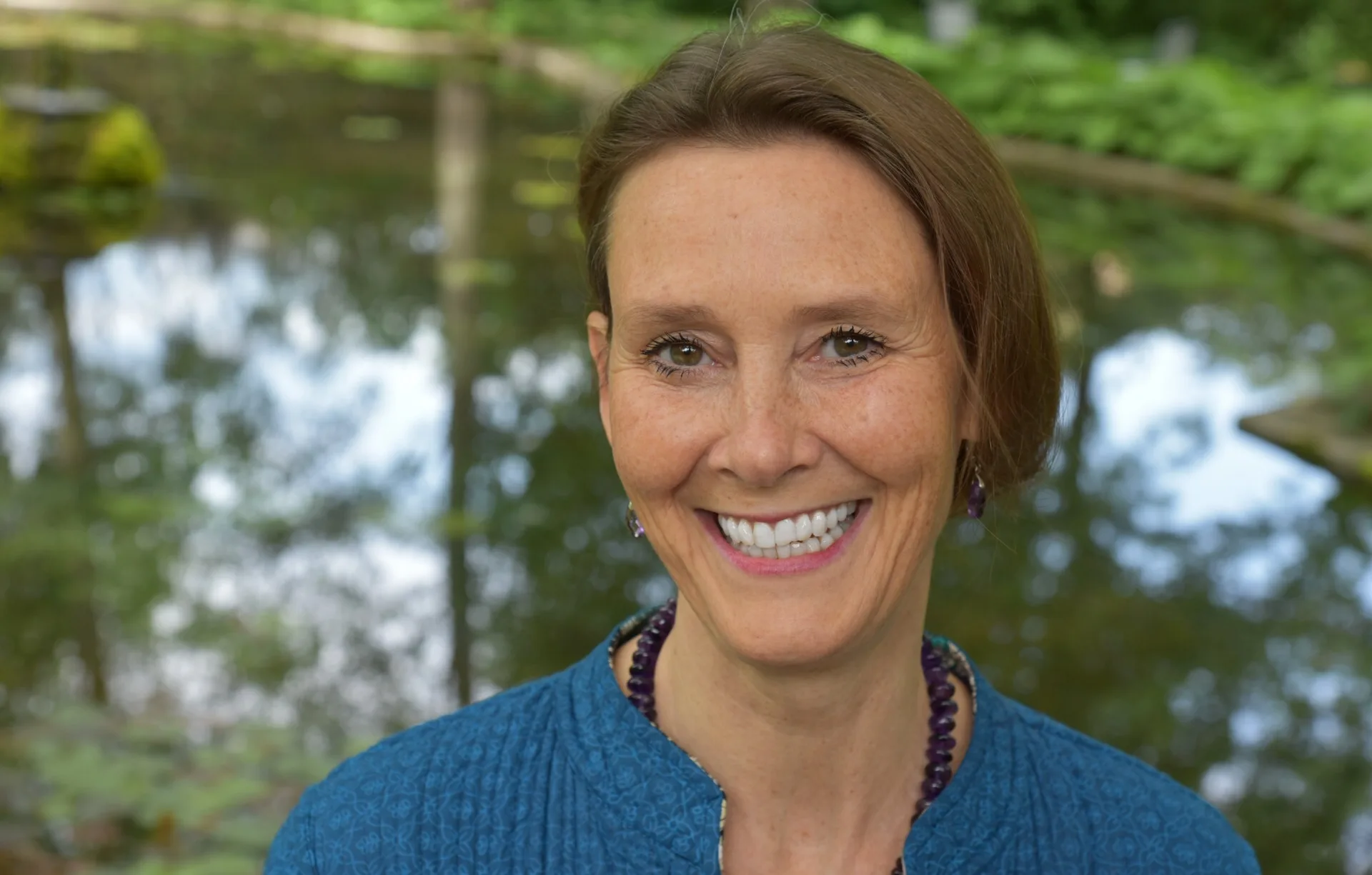 Warm portrait of Rosemarie Wagner smiling outdoors by a pond, perfectly embodying the approachable, nature-connected healer described in the article.