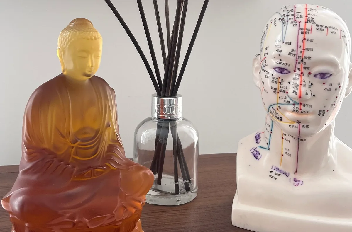 A Buddha figurine, reed diffuser, and acupuncture head model create a calm, holistic wellness atmosphere.