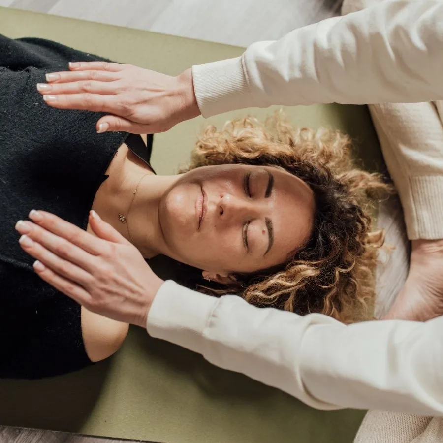 A practitioner places hands gently around a woman's head during an energy session.