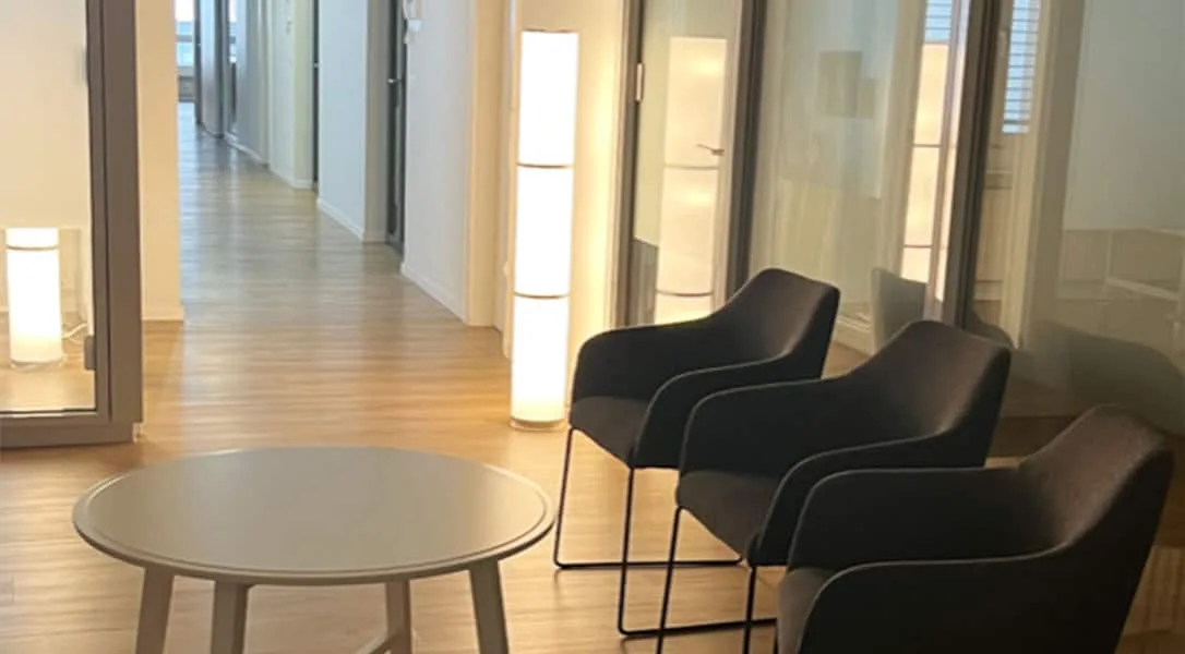 A calm modern dental practice waiting area with dark armchairs, a round table, and warm floor lamps.